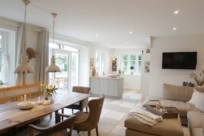 A spacious living area with a dining table, chairs, a sofa, and a kitchen in the background. - Apartment 'Kohstall' with Private Terrace, Shared Garden and Wi-Fi (Högel)