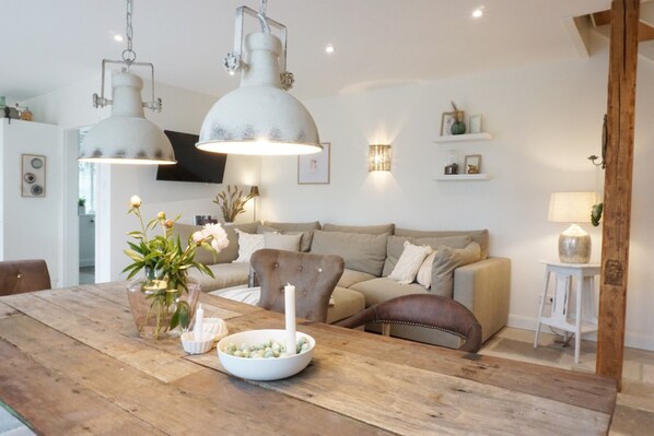 Una sala de estar acogedora con una mesa de comedor de madera, un sofá y un televisor instalado en la pared.