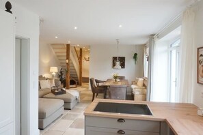 Una sala de estar moderna con un sofá, una mesa de comedor con sillas, una escalera y una zona de cocina con un lavamanos.