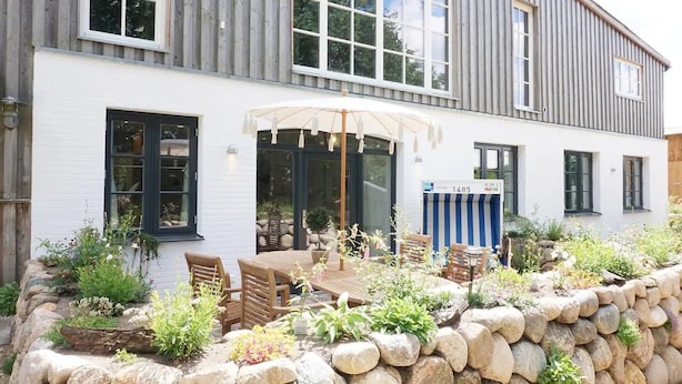 A two-story building with a patio area featuring a table and chairs, surrounded by a stone wall and various plants. - Apartment 'Lütje Orange' with Private Terrace, Shared Garden and Wi-Fi (Högel)