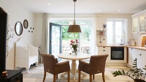 A dining area with a round table and four chairs, a kitchen with a dishwasher, and a view of greenery through the glass door. - Apartment 'Lütje Orange' with Private Terrace, Shared Garden and Wi-Fi (Högel)