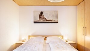 A bedroom with a large bed, two bedside tables with lamps, a wooden wardrobe, and a painting on the wall.
