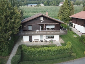 Une maison à deux étages avec un balcon, une cheminée et un petit jardin.