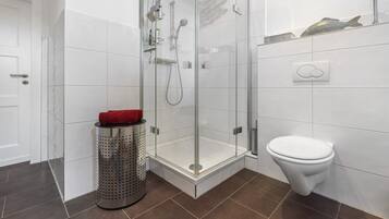 A modern bathroom with a glass-enclosed shower, a white toilet, and a tiled floor.