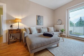 Ein Schlafzimmer mit Bett, Nachttisch, Lampe, Kunstwerk und Blick durch ein Fenster.