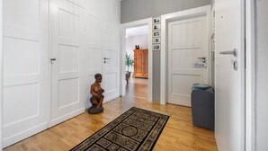 Un passadís amb portes blanques, una catifa amb dibuixos, una petita estàtua i un armari amb quadres.