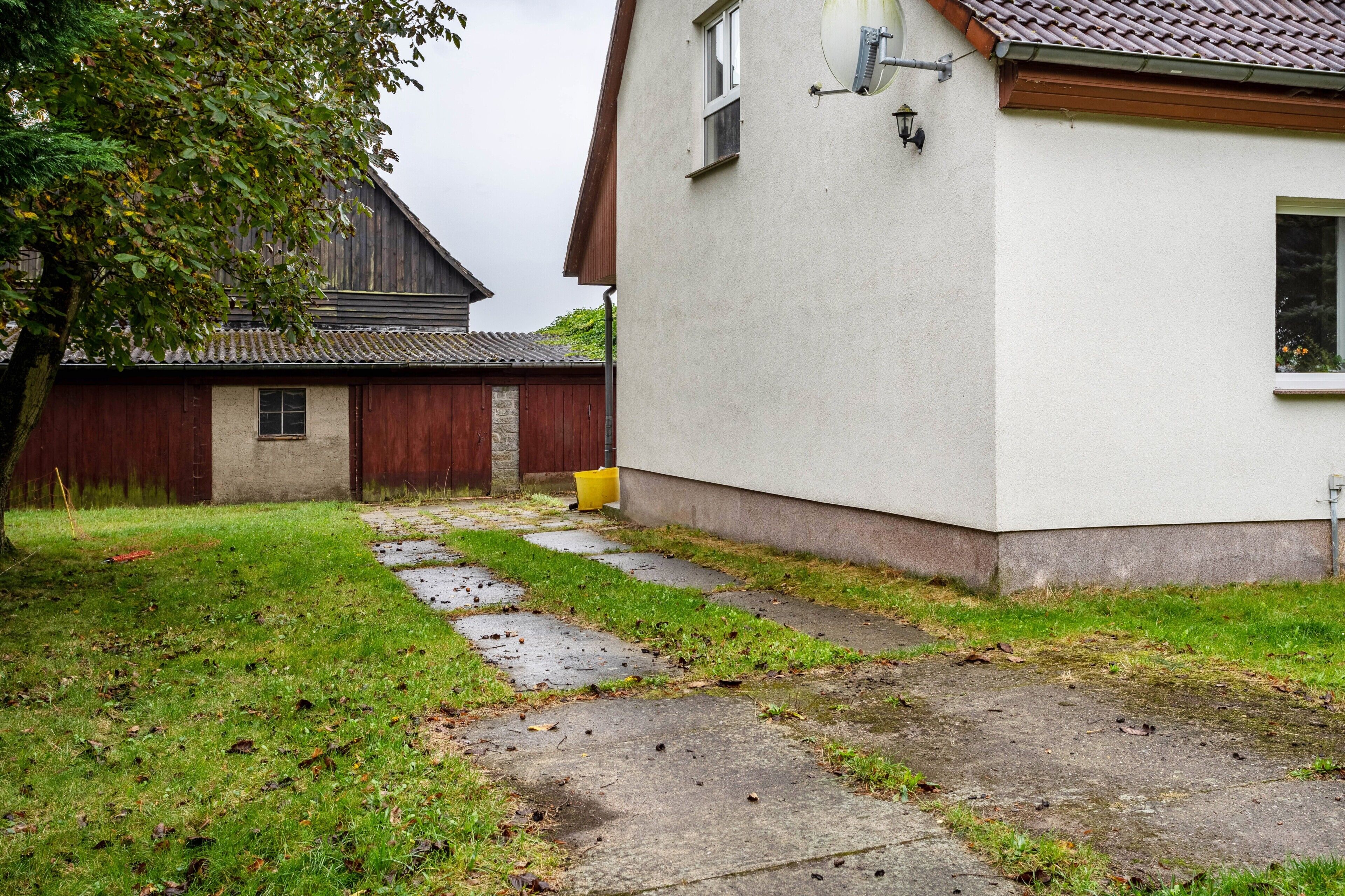 Ein Haus mit einem Betonweg, der zu einer Holztür führt, einer weißen Außenwand und einer Satellitenschüssel.
