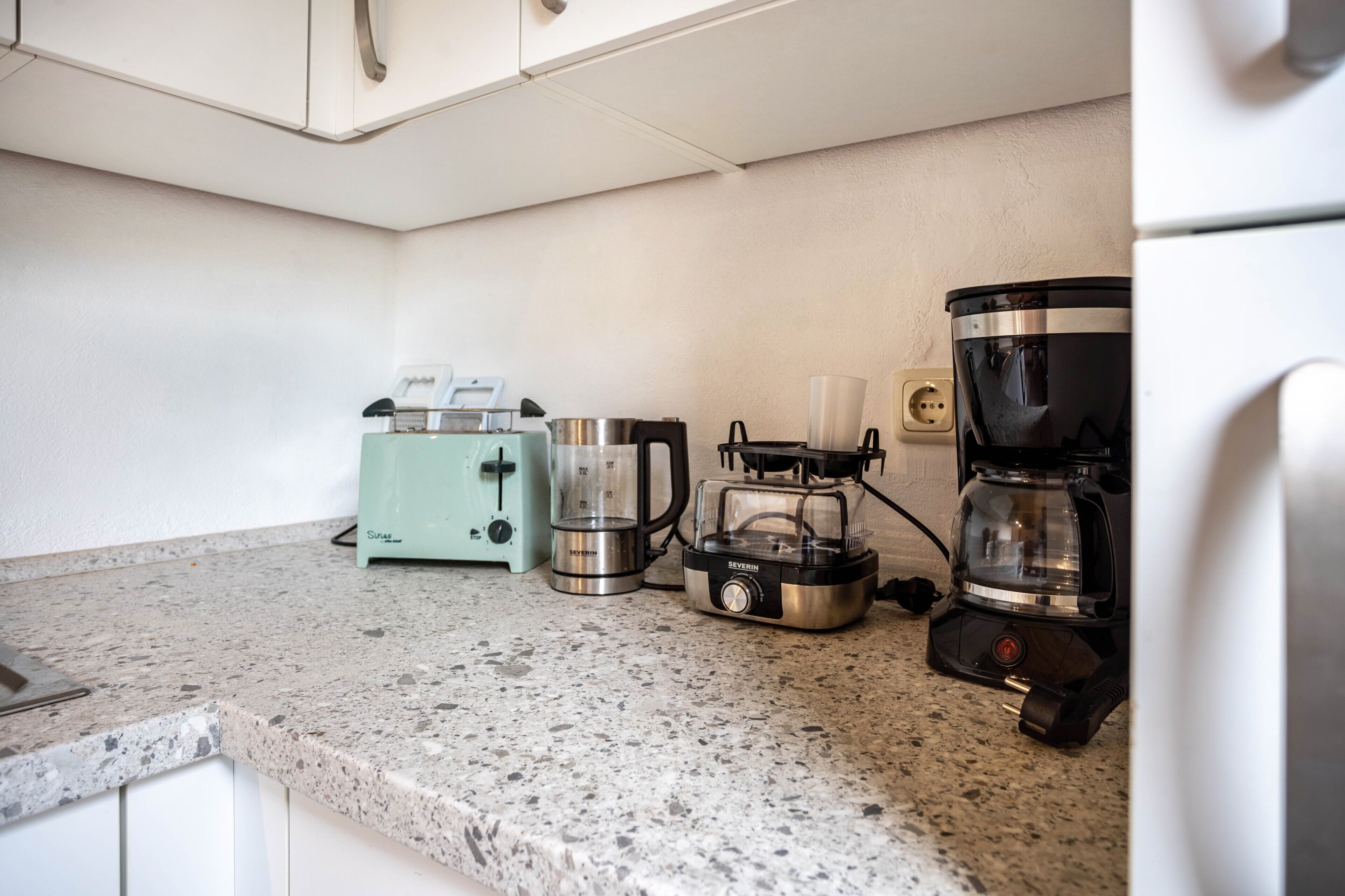 Een keuken met een toaster, blender en koffiezetapparaat op een granieten aanrecht.