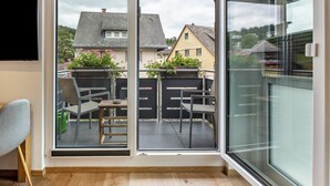 A room with a sliding glass door leading to an outdoor balcony with chairs and a table. - Maisonette Apartment with Mountain View, Balcony, and Wi-Fi (Lenzkirch)