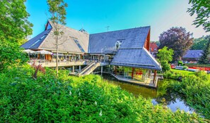 Ein Gebäude mit Satteldach und einem Wasserlauf davor, mit einer Treppe, die zu einer oberen Ebene führt.