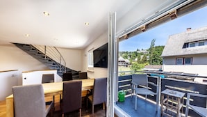 A modern interior with a dining area, staircase, and a view of a residential neighborhood. - Maisonette Apartment with Mountain View, Balcony, and Wi-Fi (Lenzkirch)