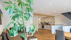 A modern living space with a wooden floor, a dining area, and a kitchen in the background. - Maisonette Apartment with Mountain View, Balcony, and Wi-Fi (Lenzkirch)
