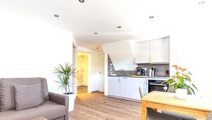 A modern living room with a sofa, a wooden coffee table, and a dining table with chairs. There is a kitchen area with white cabinets and a countertop. - Apartment 'Haslach Ground Floor' with Mountain View and Wi-Fi (Lenzkirch)