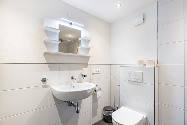 Un baño moderno con lavamanos, espejo y retrete blancos.