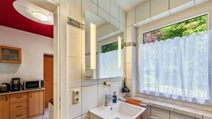 Un baño con lavamanos blanco, espejo y ventana con cortinas.