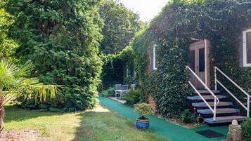 A garden pathway leading to a staircase with a metal railing, surrounded by lush greenery and a small tree in a pot.