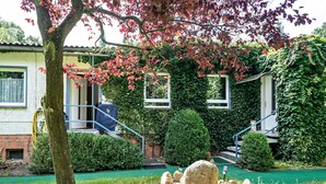 Una casa con jardín delantero, un árbol de hojas rojas y una construcción de piedra.