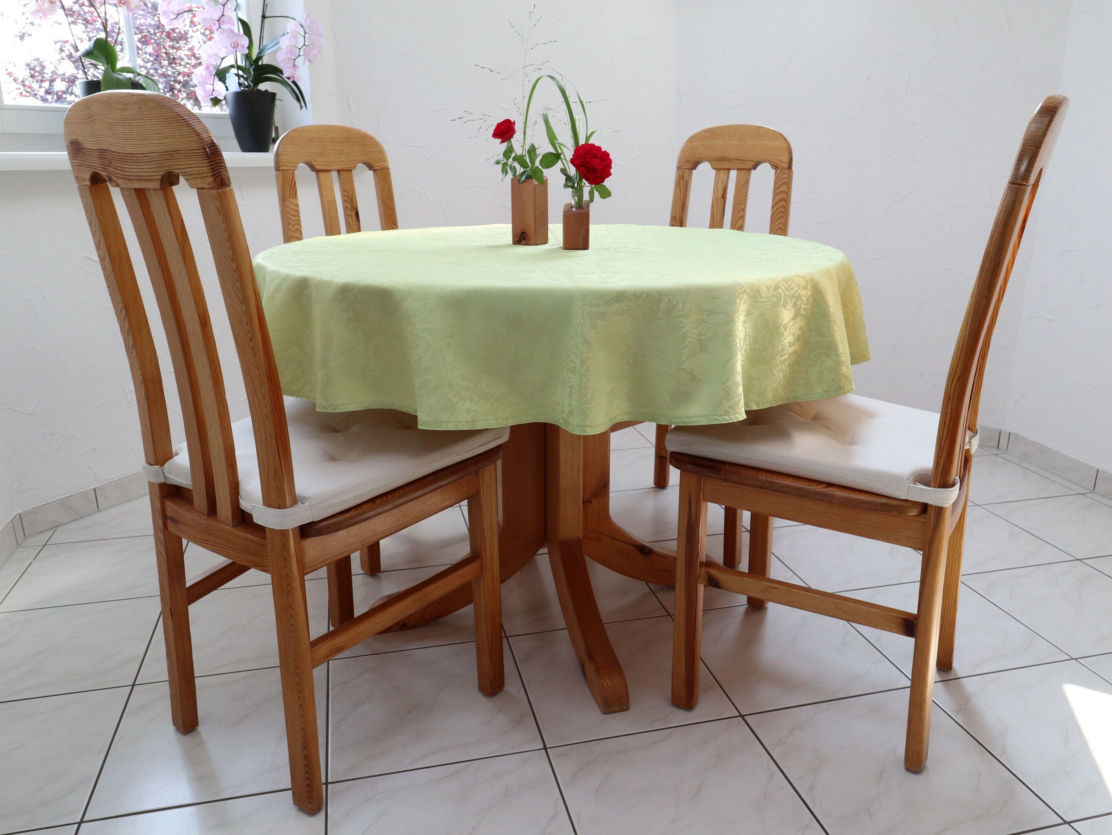 Ein runder Holztisch mit grüner Tischdecke, umgeben von vier Holzstühlen mit gepolsterten Sitzen.