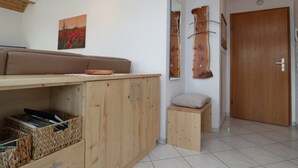 Una habitación con un banco de madera, un taburete pequeño, un armario con cestas tejidas y una puerta.