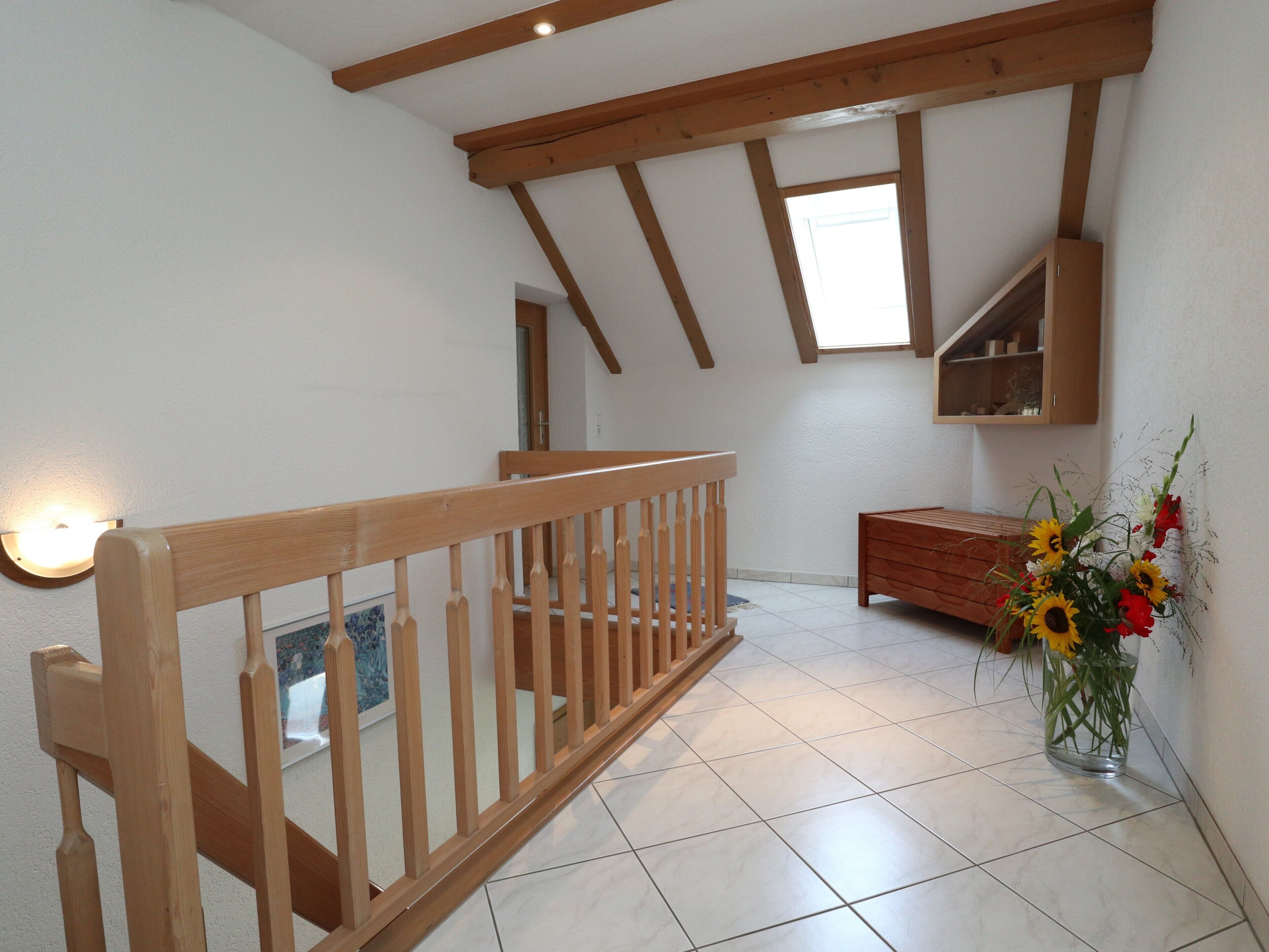 Une pièce avec un escalier en bois, une armoire en bois et un vase rempli de fleurs.