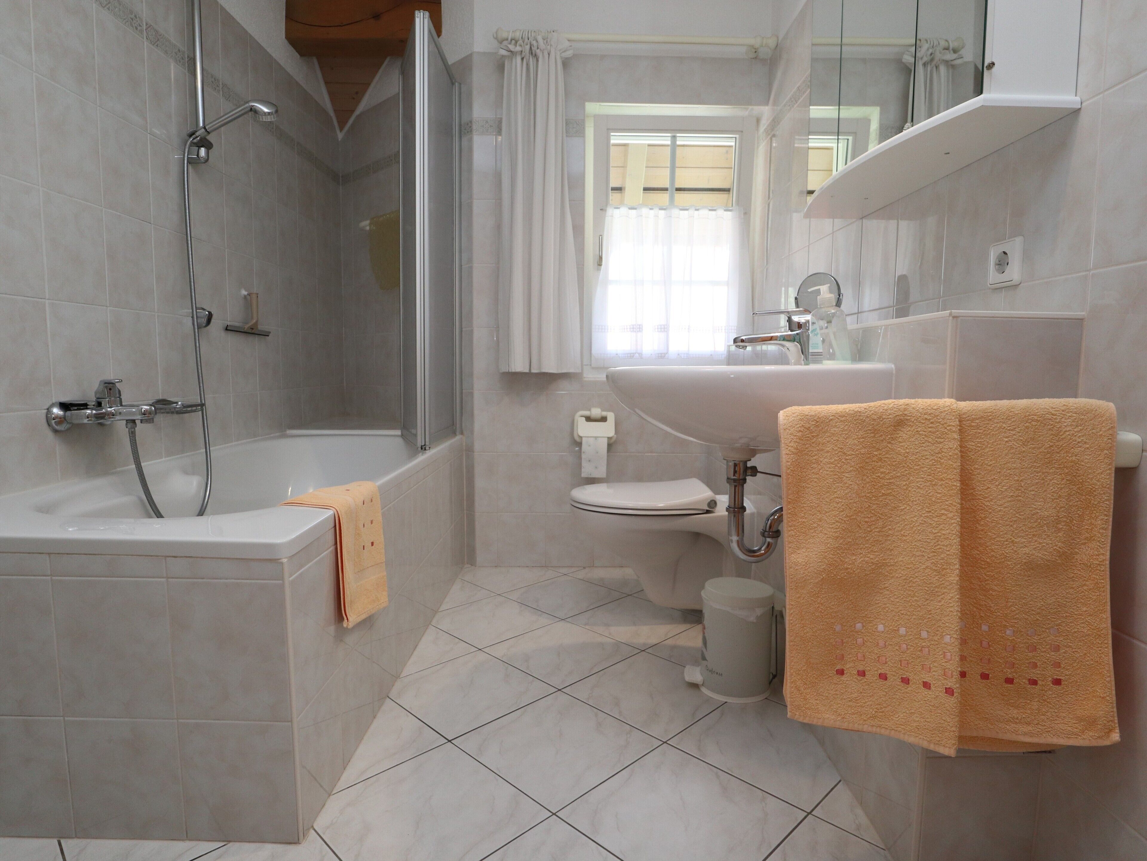 A bathroom with a bathtub, shower, toilet, sink, and a window with curtains.