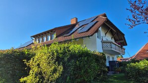 Una casa de dos pisos con techo inclinado, paneles solares y un balcón con flores.