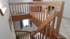 Una escalera de madera con barandilla, una ventana con cortinas azules y una planta en maceta con flores.