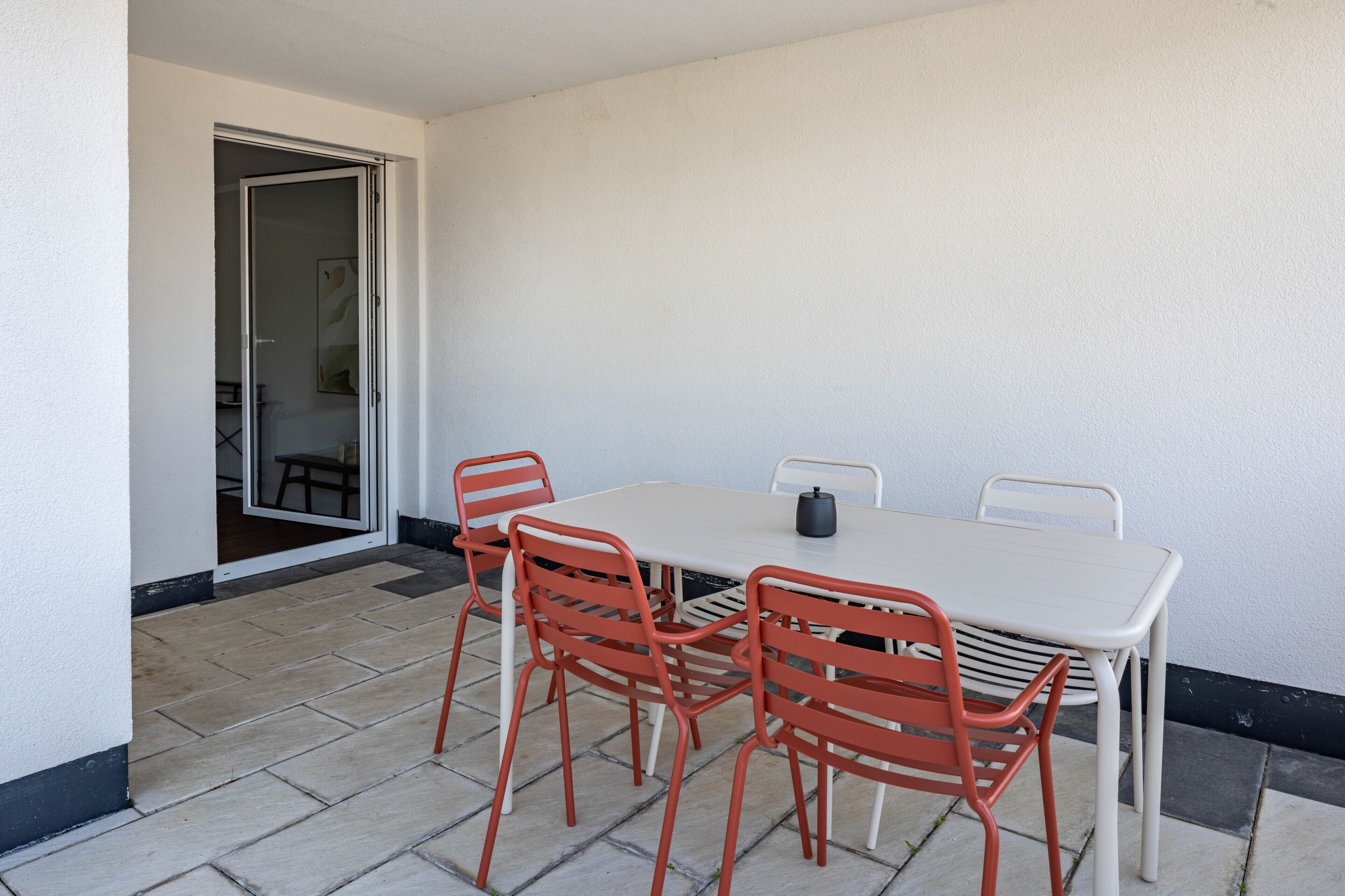 Un espace patio avec une table et quatre chaises, une porte donnant sur une pièce et un sol carrelé.
