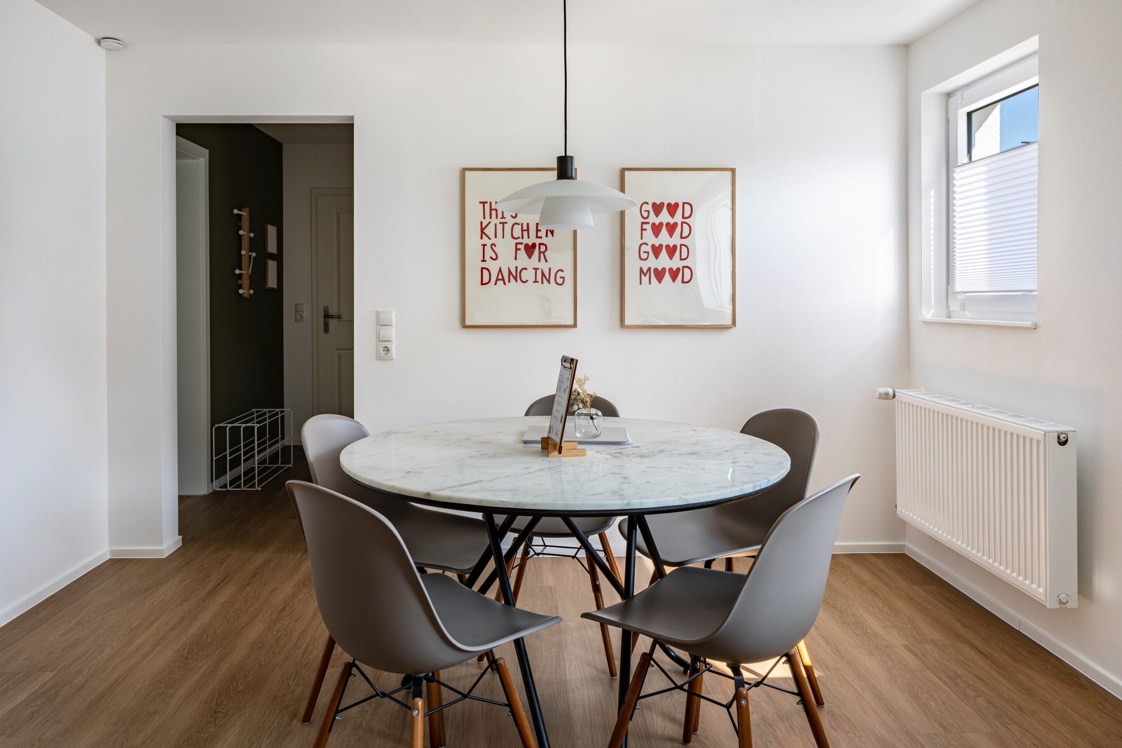 Un coin repas comprenant une table ronde, quatre chaises, un luminaire suspendu et deux citations encadrées accrochées au mur.