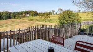 A patio with a table and chairs, a wooden fence, and a view of a rural landscape.