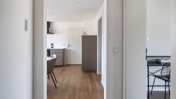 A modern kitchen with white cabinets, a grey refrigerator, and a dining area with a black chair.