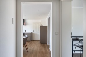 A modern kitchen with white cabinets, a grey refrigerator, and a dining area with a black chair. - Apartment 'Zimis Hofnest' with Mountain View, Private Terrace and Wi-Fi (Freiamt)