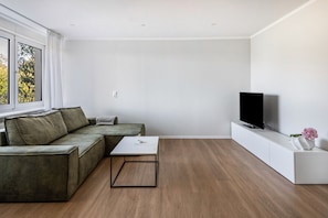 Uma sala de estar moderna com um sofá seccional, uma mesa de centro, uma televisão de tela plana e um console branco.