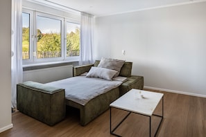 Quarto moderno com cama, uma mesinha e janela com vista para árvores.
