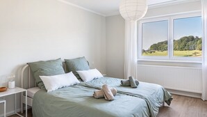 A bedroom with a bed, pillows, a nightstand, a lamp, and a window with a view of a landscape.