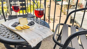 A table with a cheese plate, crackers, and two glasses of red wine on a balcony with metal railings.