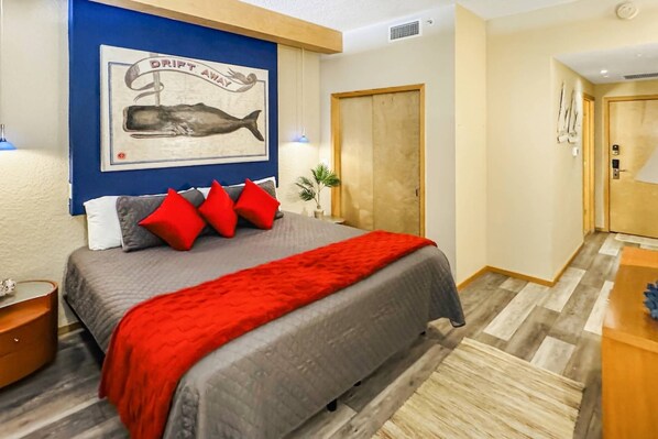 Un dormitorio con cama, una manta roja, un cuadro de una ballena y una puerta de madera.