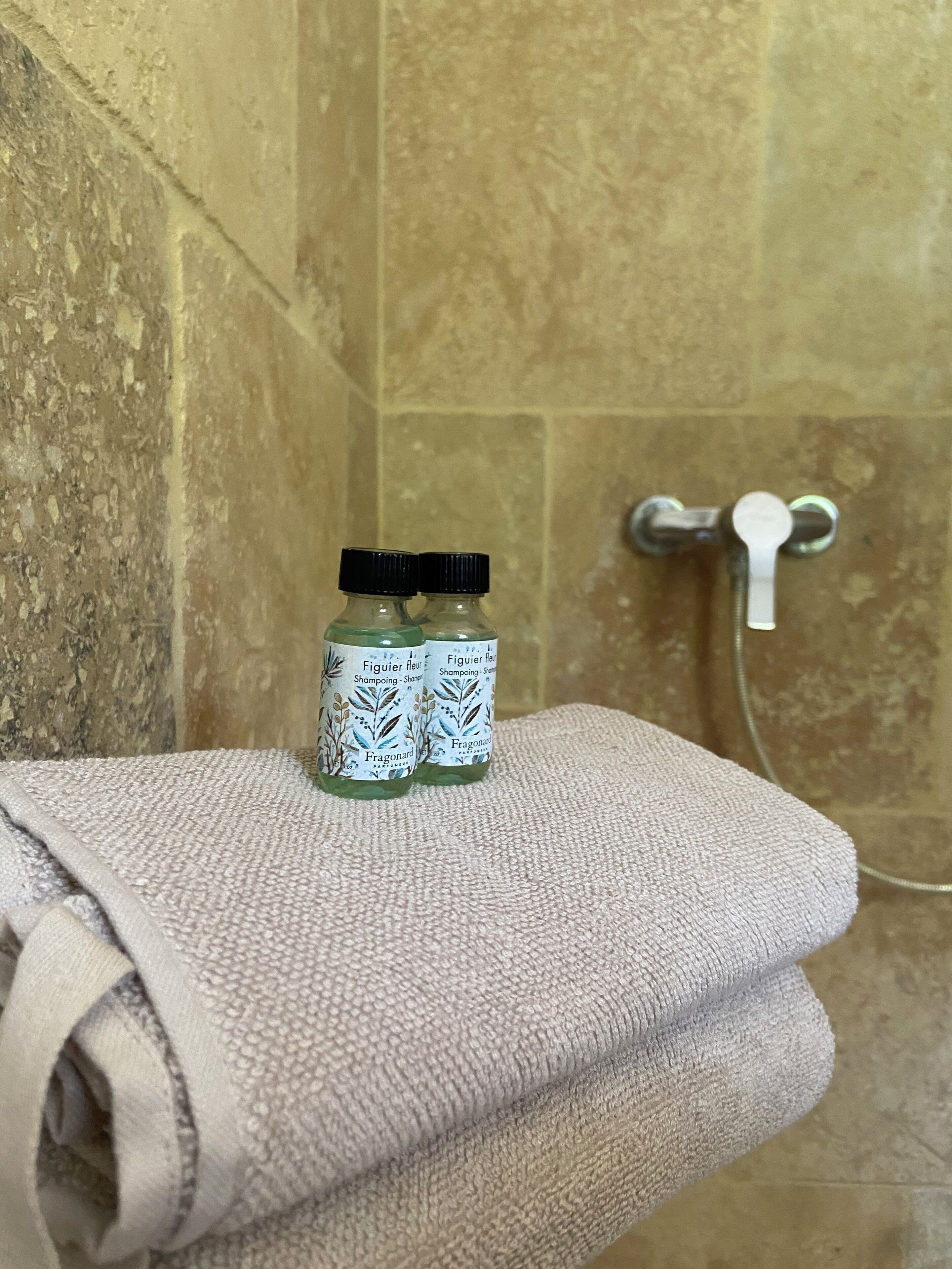 A bathroom with a towel rack holding a folded towel and two bottles of shampoo on a textured surface.