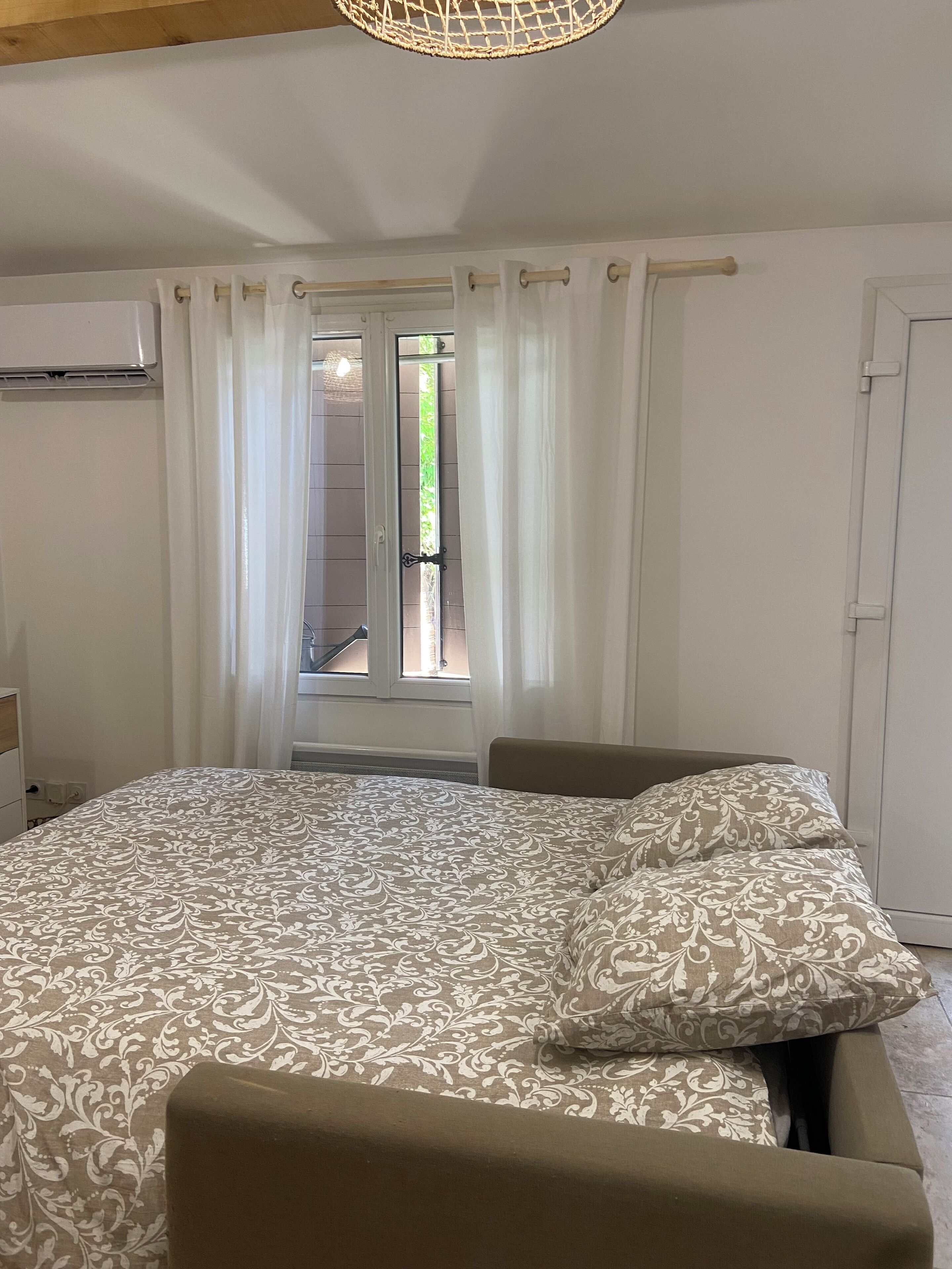 A bedroom with a bed, a window with curtains, a door, and an air conditioning unit.