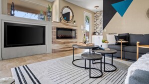 A living room with a fireplace, a TV, a sofa, and a coffee table. - Desert Playhouse | Pool & Hot Tub • Arcade • Golf (Chandler)