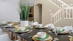 A dining area with a long table set for a meal, a potted plant, and a staircase in the background. - Desert Playhouse | Pool & Hot Tub • Arcade • Golf (Chandler)