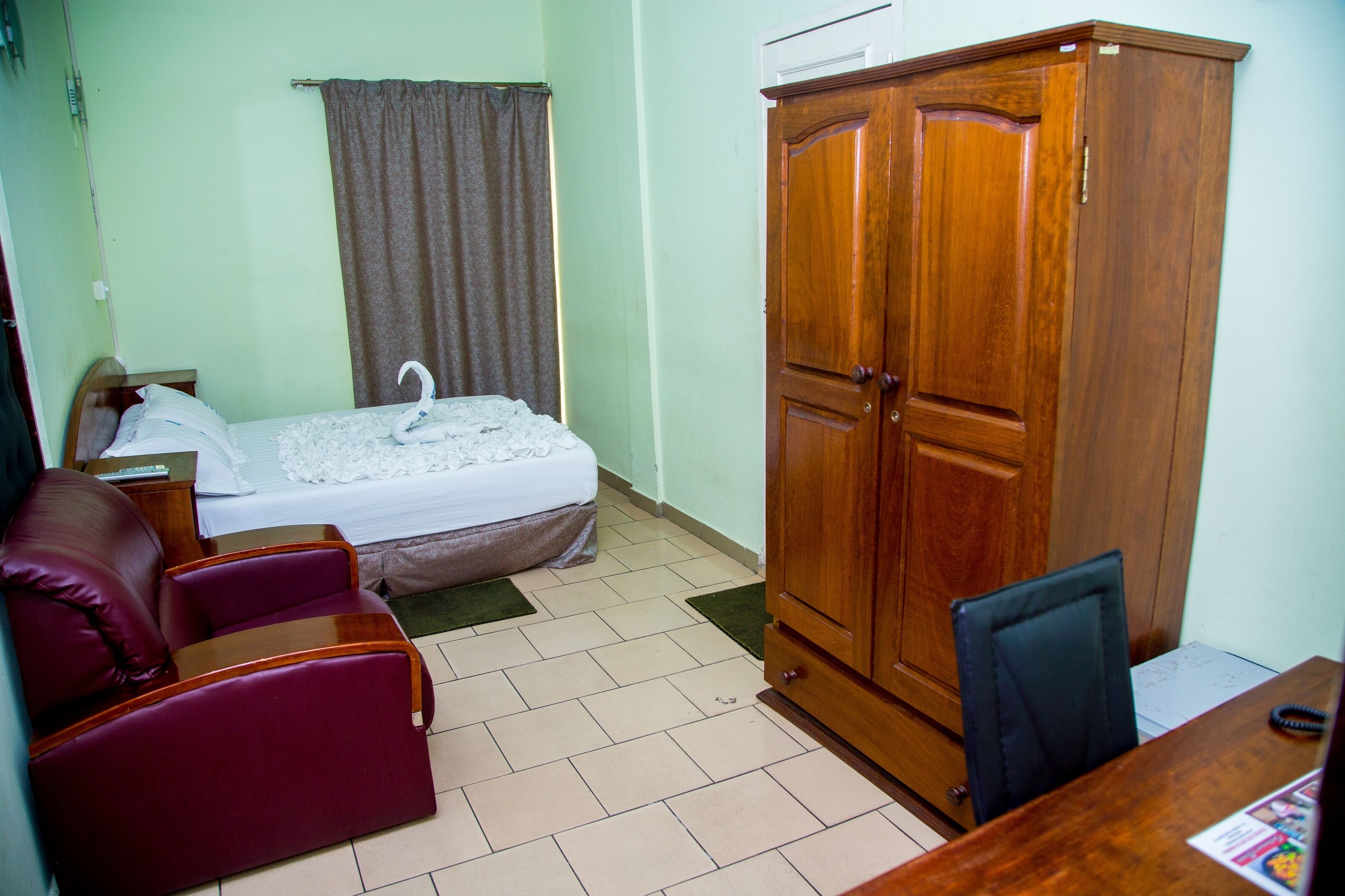 A room with a bed, a wooden wardrobe, a red sofa, and a desk with a chair.
