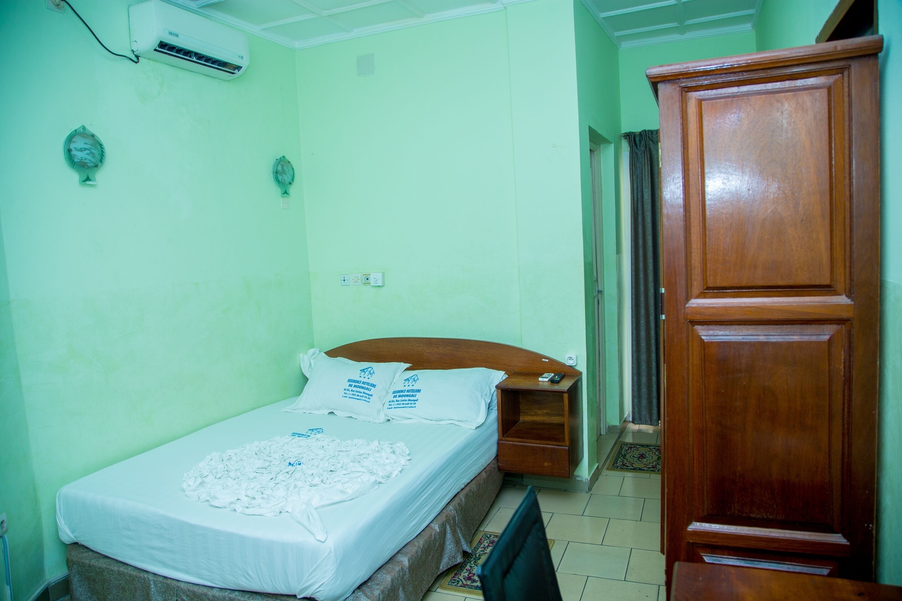 A room with a bed, a wooden wardrobe, and a wall-mounted air conditioner.