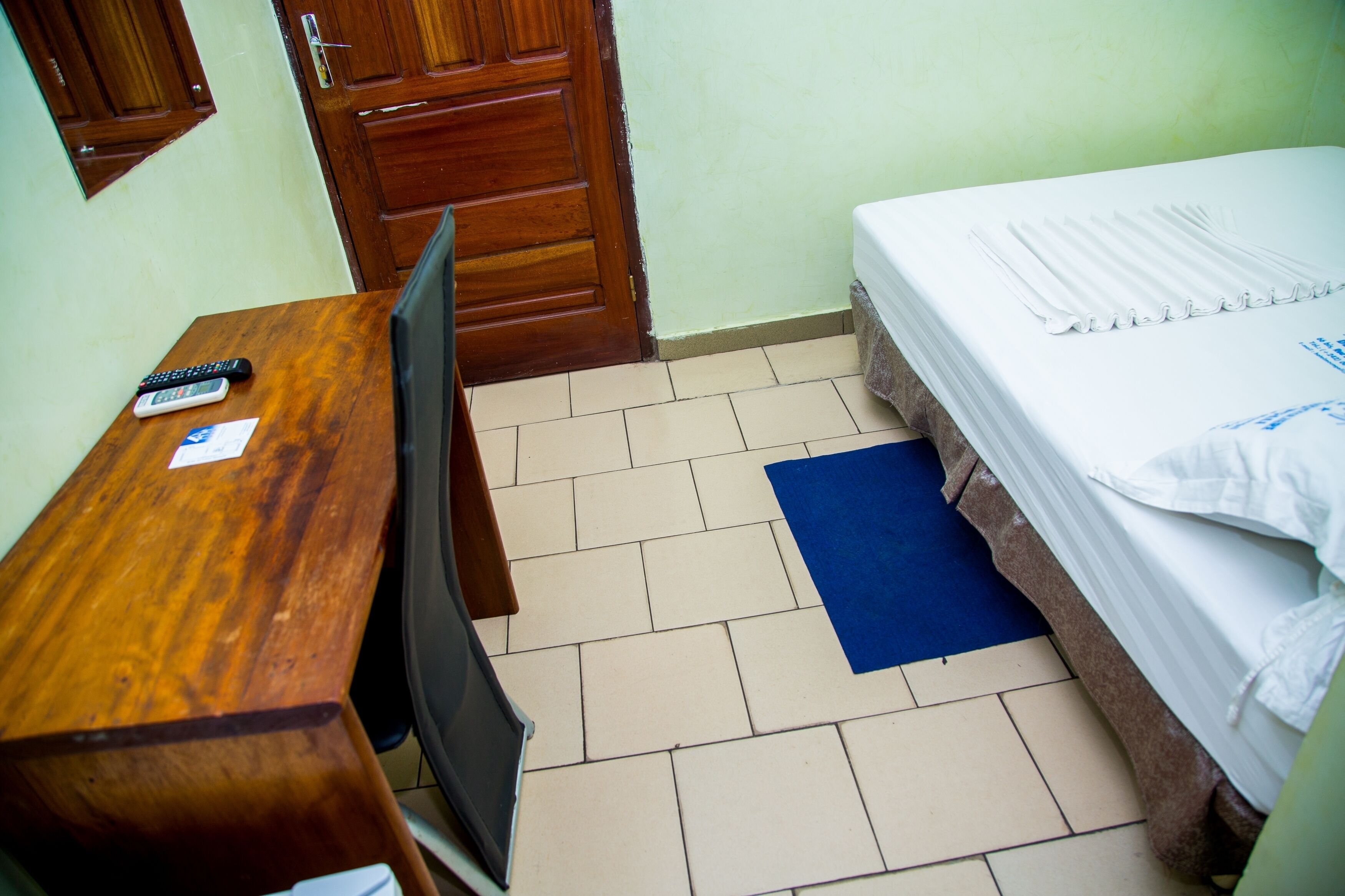 Una habitación pequeña con un escritorio de madera, una silla, una cama con un colchoneta azul y una puerta de madera.