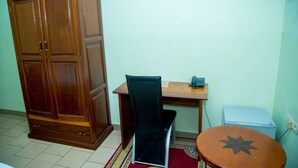 Una habitación con un armario de madera, un escritorio con silla, una mesita y un enchufe.