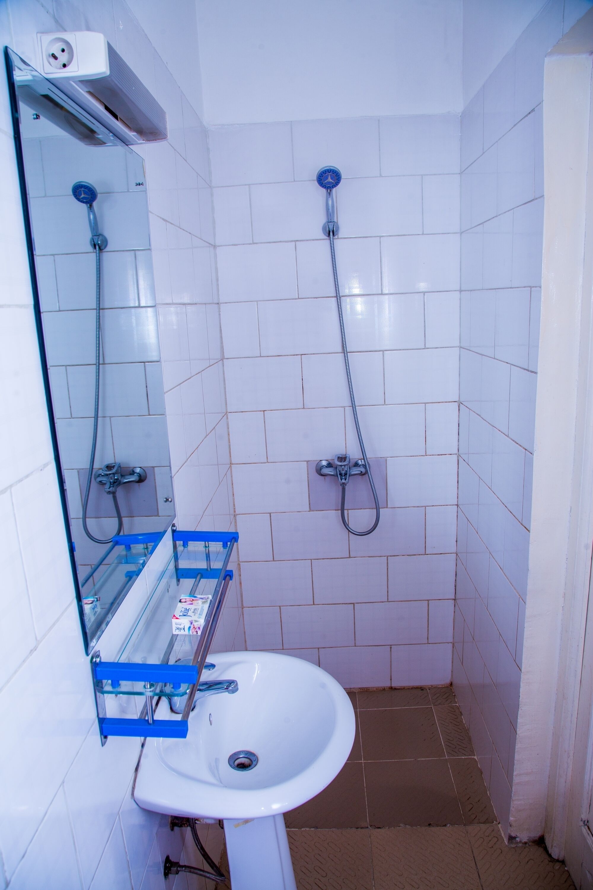 Un bagno piccolo rivestito di piastrelle bianche, con un lavandino bianco, uno specchio e due soffioni doccia.