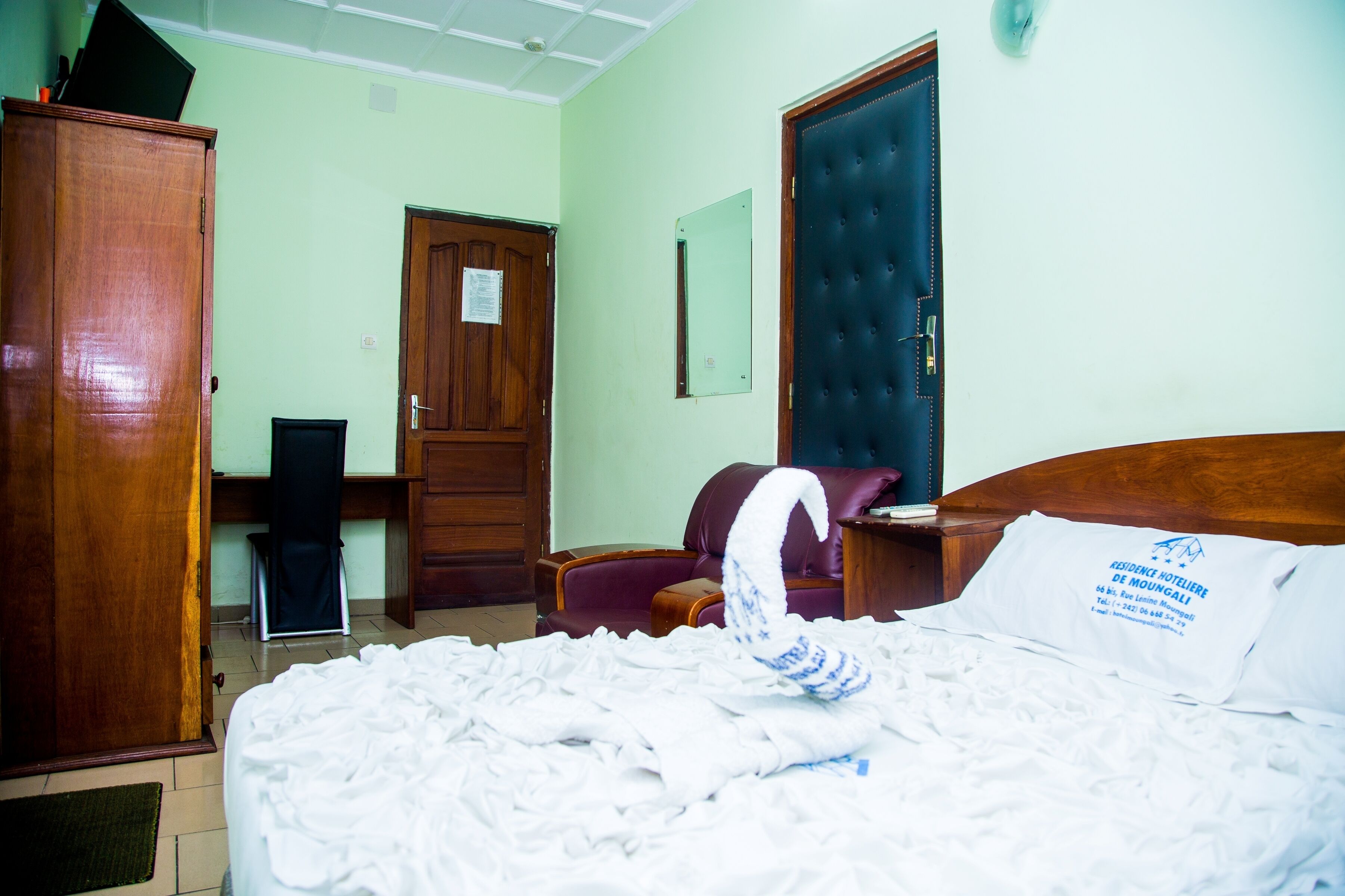 A hotel room with a bed, a wardrobe, a desk, and a door.