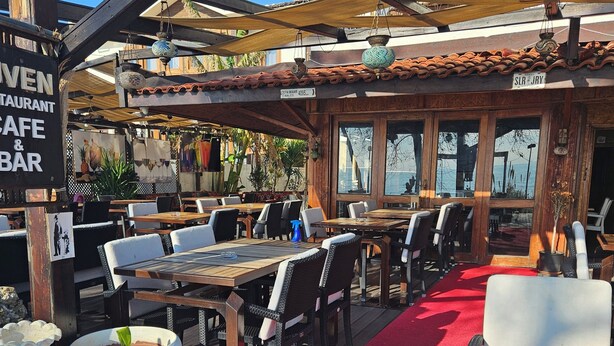 An outdoor dining area with wooden tables and chairs, a red carpet path, and a sign indicating a restaurant and bar. - Güven hotel (Manavgat)
