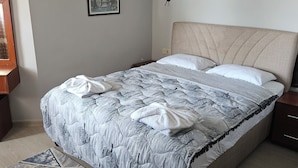 A neatly made bed with a patterned duvet, a bedside table, a wall-mounted lamp, and a framed picture on the wall. - Güven hotel (Manavgat)