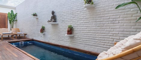 A pool area with a white brick wall, wooden deck, and a statue.